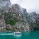 A tour boat sailing past a rocky cliff face, dotted with foliage